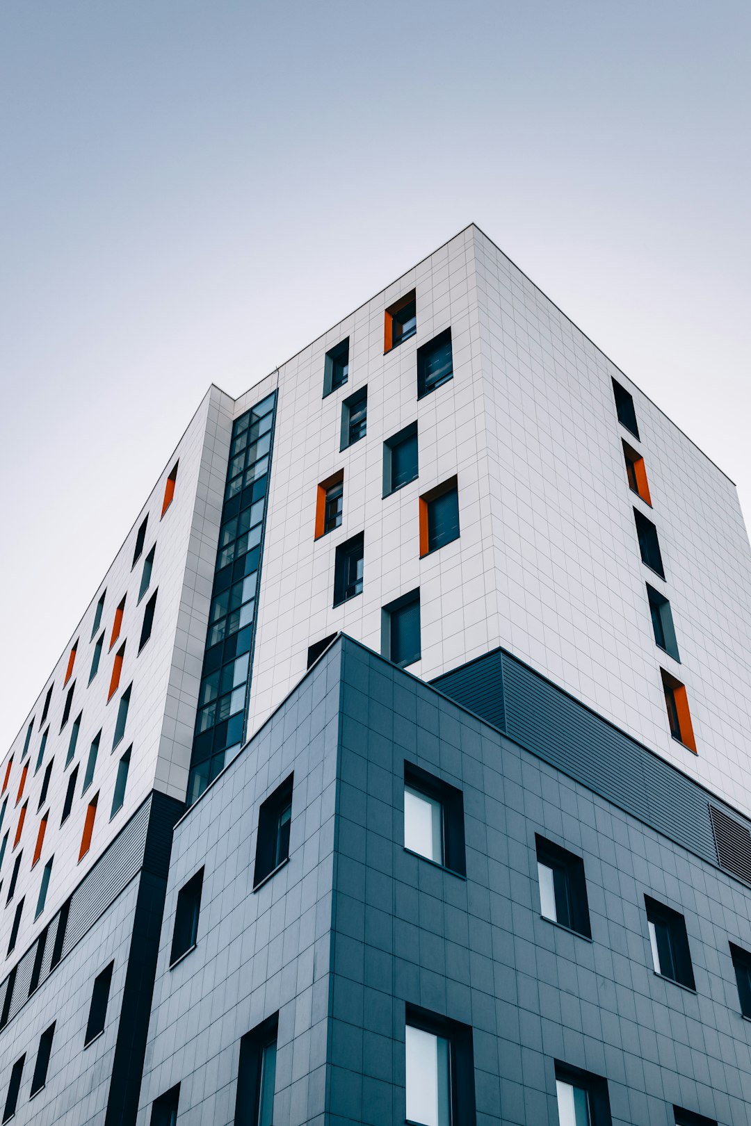 A modern building with white and grey tiled facades and orange window accents