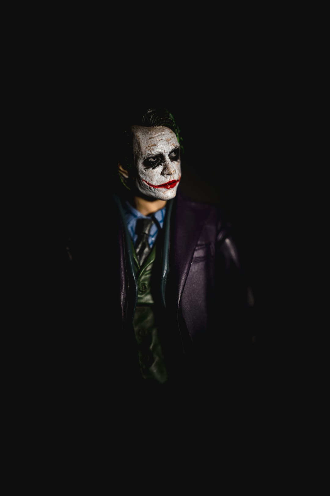 A figurine with white face paint and red lipstick wearing a purple suit